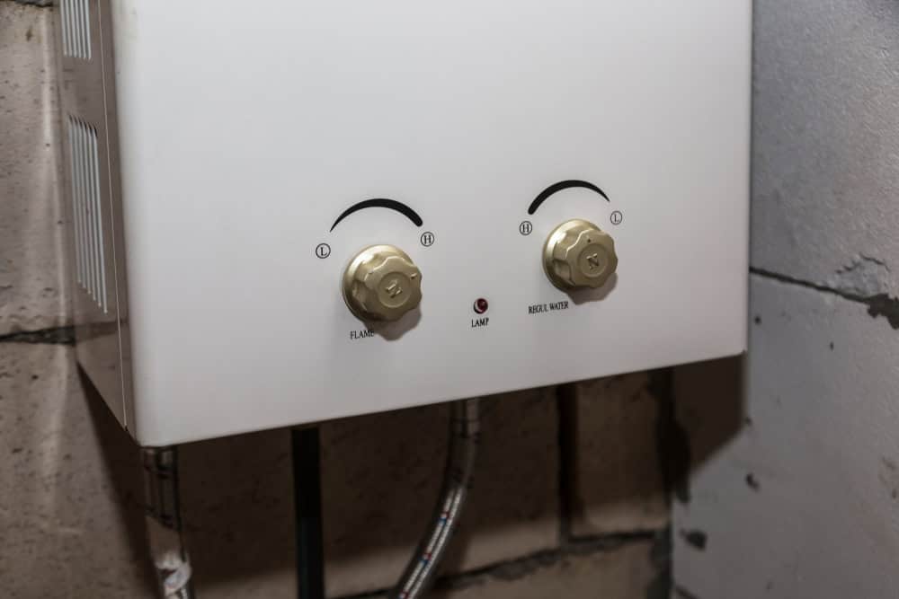 Close-up of a white wall-mounted water heater control panel with two round knobs labeled "Flow" and "Heat" on a textured concrete wall. Ideal for residential plumbers, it features a small red indicator light labeled "Lamp" between the knobs, ensuring efficient installation and maintenance.