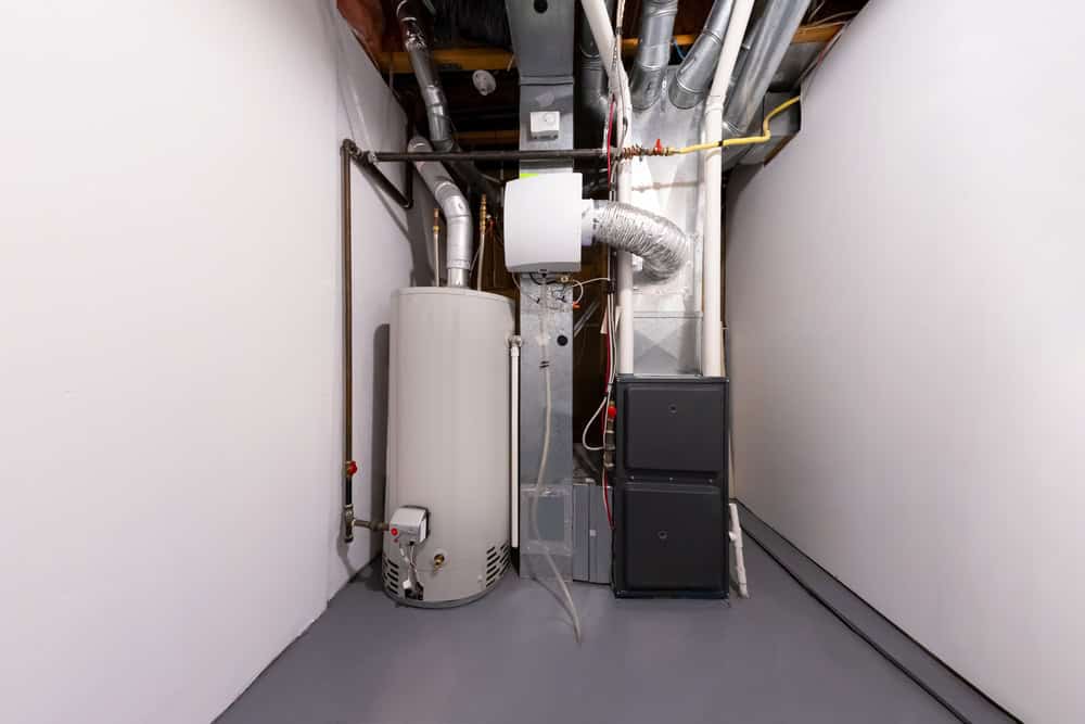 A basement utility area with a furnace, air ducts, and a water heater. The walls are white, the floor is gray, and exposed pipes line the ceiling. Ideal for a residential plumber specializing in mini split AC installations to work efficiently in this organized space.