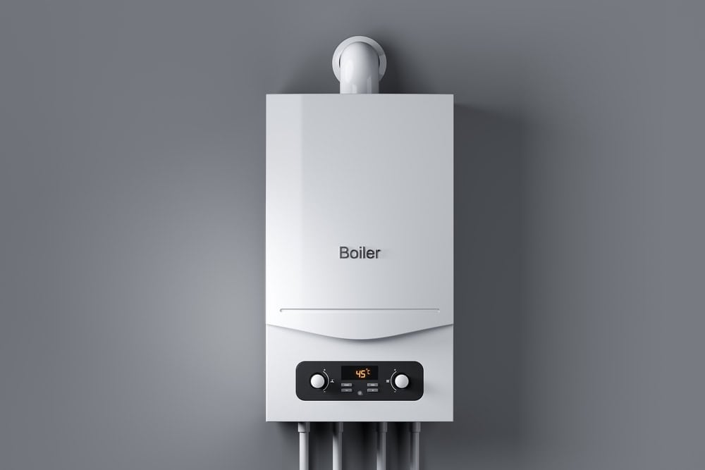 A white boiler from our trusted boiler services is mounted on a gray wall. It features a digital display showing 45 degrees, with control knobs below. Several pipes flow from the bottom of the unit, expertly installed by our skilled plumber team.