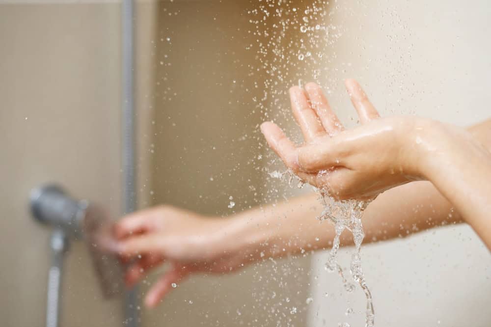 A person adjusting a shower knob with one hand like a skilled plumber while catching splashing water with the other.